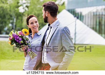 Stock Photography - Young attractive business couple walking in park while the woman is holding boquet of flowers. Fotosearch