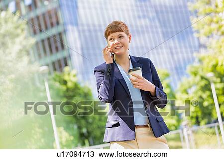 Young attractive businessman holding a cup of coffee while smiling and talking on smartphone View Large Photo Image Stock Image - Young attractive businessman holding a cup of coffee while smiling and talking on smartphone . Fotosearch