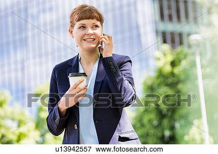 Young attractive businessman holding a cup of coffee while smiling and talking on smartphone View Large Photo Image Stock Photo - Young attractive businessman holding a cup of coffee while smiling and talking on smartphone . Fotosearch