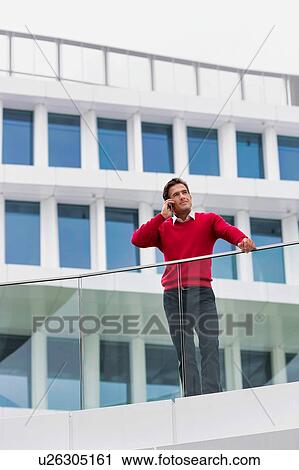 Stock Image - Young attractive businessman talking on smartphone in rooftop. Fotosearch