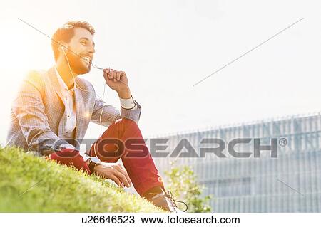 Young attractive businessman talking on smartphone with earphones on while sitting on the grass View Large Photo Image Stock Image - Young attractive businessman talking on smartphone with earphones on while sitting on the grass. Fotosearch