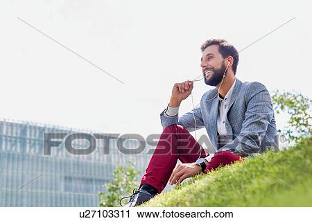 Young attractive businessman talking on smartphone with earphones on while sitting on the grass View Large Photo Image Stock Image - Young attractive businessman talking on smartphone with earphones on while sitting on the grass. Fotosearch