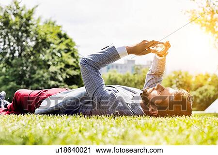Stock Image - Young attractive businessman using digital tablet while lying on the grass. Fotosearch