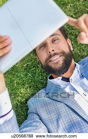 Young attractive businessman using digital tablet while lying on the grass View Large Photo Image Stock Photo - Young attractive businessman using digital tablet while lying on the grass. Fotosearch