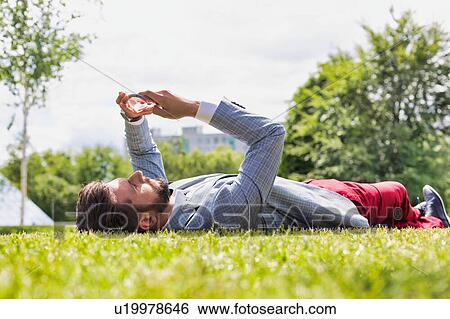 Young attractive businessman using digital tablet while lying on the grass View Large Photo Image Stock Photograph - Young attractive businessman using digital tablet while lying on the grass. Fotosearch