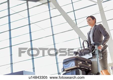 Stock Photography - Young attractive businesswoman pushing baggage cart for check in at airport. Fotosearch