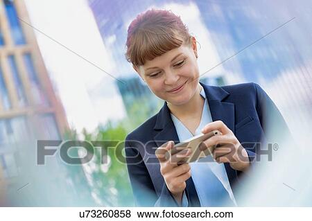 Stock Photo - Young attractive businesswoman smiling while using smartphone . Fotosearch