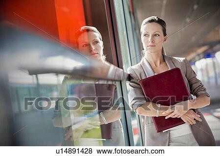 Young attractive businesswoman standing and holding document while looking through the window View Large Photo Image Stock Photo - Young attractive businesswoman standing and holding document while looking through the window. Fotosearch