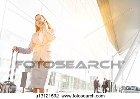 Young attractive businesswoman talking on smartphone while walking with her suitcase in airport View Large Photo Image Stock Image - Young attractive businesswoman talking on smartphone while walking with her suitcase in airport. Fotosearch