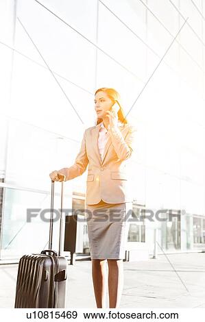 Young attractive businesswoman talking on smartphone while walking with her suitcase in airport View Large Photo Image Stock Photo - Young attractive businesswoman talking on smartphone while walking with her suitcase in airport. Fotosearch