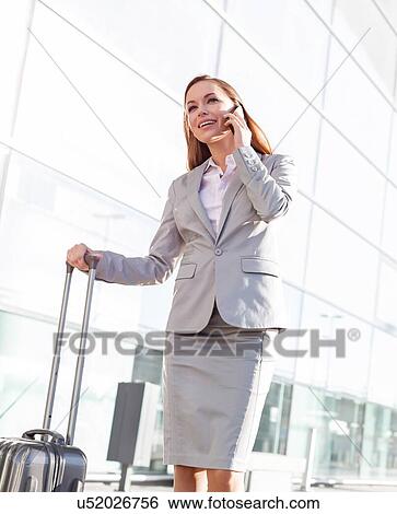 Young attractive businesswoman talking on smartphone while walking with her suitcase in airport View Large Photo Image Stock Photograph - Young attractive businesswoman talking on smartphone while walking with her suitcase in airport. Fotosearch