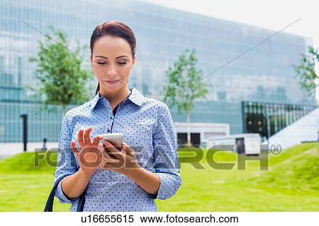 Stock Photography - Young attractive businesswoman using smartphone outdoors. Fotosearch