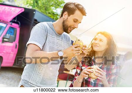 Young attractive couple eating hamburgers against food truck with lens flare in background View Large Photo Image Stock Image - Young attractive couple eating hamburgers against food truck with lens flare in background. Fotosearch