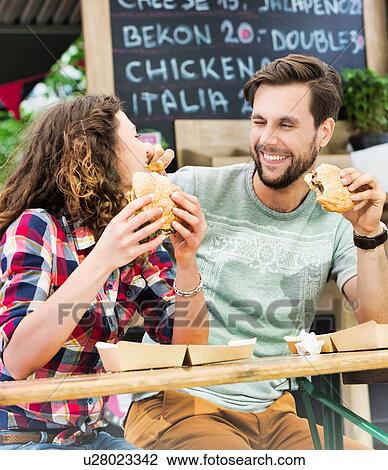 Young attractive couple eating hamburgers against food truck with lens flare in background View Large Photo Image Stock Image - Young attractive couple eating hamburgers against food truck with lens flare in background. Fotosearch