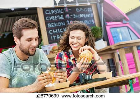 Young attractive couple eating hamburgers against food truck View Large Photo Image Stock Photo - Young attractive couple eating hamburgers against food truck. Fotosearch