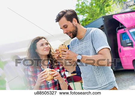 Stock Photo - Young attractive couple eating hamburgers against food truck. Fotosearch