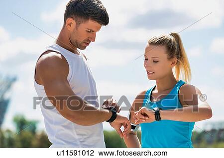 Young attractive couple looking at their watch in park View Large Photo Image Stock Image - Young attractive couple looking at their watch in park. Fotosearch