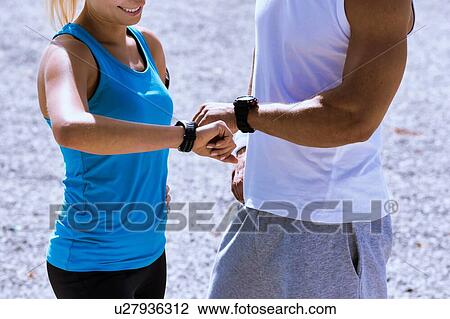 Young attractive couple looking at their watch in park View Large Photo Image Stock Image - Young attractive couple looking at their watch in park. Fotosearch