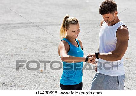 Stock Photo - Young attractive couple looking at their watch in park. Fotosearch