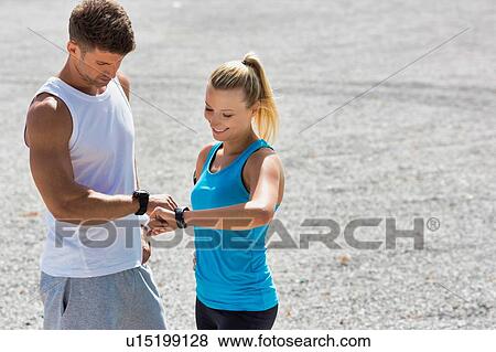Stock Photo - Young attractive couple looking at their watch in park. Fotosearch