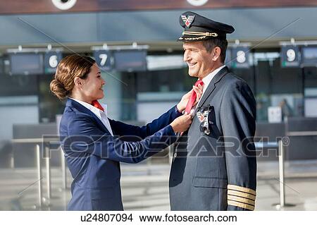 Picture - Young attractive flight attendant adjusting pilot neck tie in airport. Fotosearch