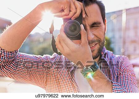 Stock Image - Young attractive man holding camera and taking photo . Fotosearch