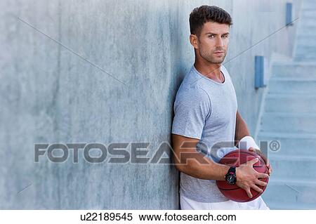 Stock Photography - Young attractive man leaning on wall while holding ball. Fotosearch