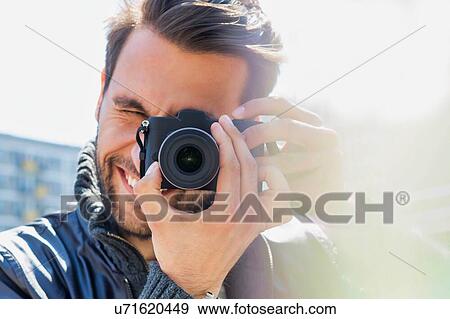 Stock Photo - Young attractive man photographing the beautiful views in the city with lens flare in background. Fotosearch