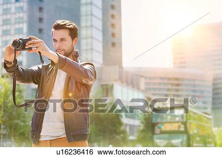 Young attractive man photographing the beautiful views in the city with lens flare in background View Large Photo Image Stock Photograph - Young attractive man photographing the beautiful views in the city with lens flare in background. Fotosearch