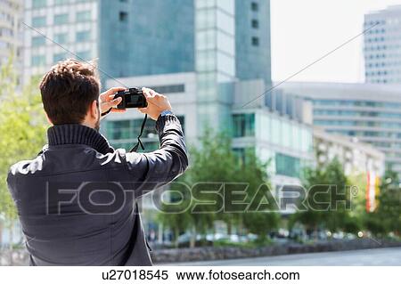 Stock Photography - Young attractive man photographing the beautiful views in the city with lens flare in background. Fotosearch