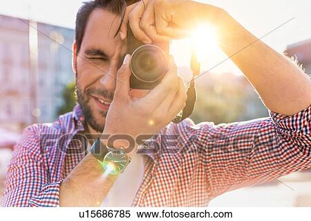 Young attractive man standing and holding camera while taking photo with lens flare View Large Photo Image Stock Photography - Young attractive man standing and holding camera while taking photo with lens flare. Fotosearch