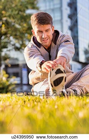 Stock Image - Young attractive man stretching his legs in park. Fotosearch