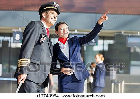 Picture - Young attractive stewardess pointing aircraft with the pilot in airport. Fotosearch