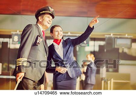 Stock Photography - Young attractive stewardess pointing aircraft with the pilot in airport. Fotosearch