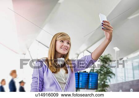 Stock Photo - Young attractive teenage girl taking selfie in airport. Fotosearch