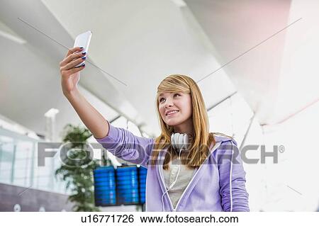 Stock Photograph - Young attractive teenage girl taking selfie in airport. Fotosearch