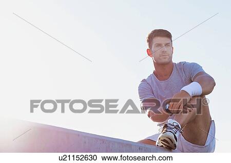 Stock Image - Young attractive thoughtful man sitting and wearing sports wear. Fotosearch