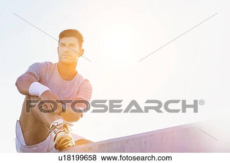 Stock Photo - Young attractive thoughtful man sitting and wearing sports wear. Fotosearch