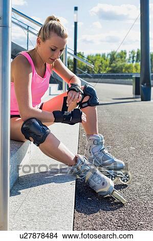 Picture - Young attractive woman adjusting safety gear while wearing rollerblades. Fotosearch