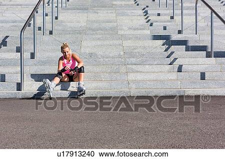 Stock Image - Young attractive woman adjusting safety gear while wearing rollerblades. Fotosearch