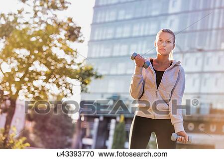Stock Image - Young attractive woman exercising and holding dumbell . Fotosearch