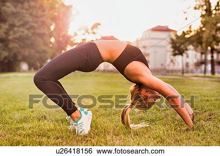 Stock Photograph - Young attractive woman exercising while bending over in park. Fotosearch