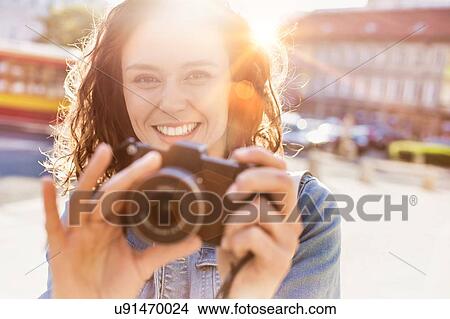 Young attractive woman holding camera and taking photo with lens flare in background View Large Photo Image Picture - Young attractive woman holding camera and taking photo with lens flare in background. Fotosearch