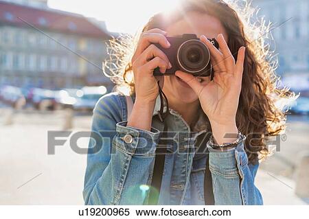Stock Photography - Young attractive woman holding camera and taking photo . Fotosearch