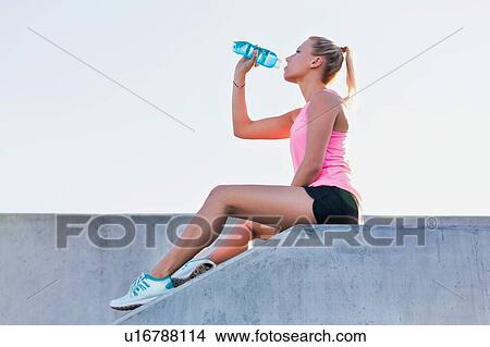 Picture - Young attractive woman sitting while drinking energy drink . Fotosearch