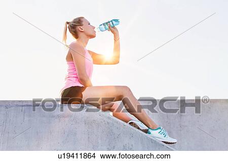 Young attractive woman sitting while drinking energy drink View Large Photo Image Picture - Young attractive woman sitting while drinking energy drink . Fotosearch