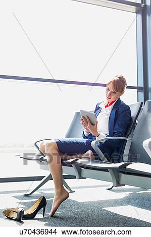 Young beautiful airport staff using digital tablet while sitting on chair during break View Large Photo Image Picture - Young beautiful airport staff using digital tablet while sitting on chair during break . Fotosearch