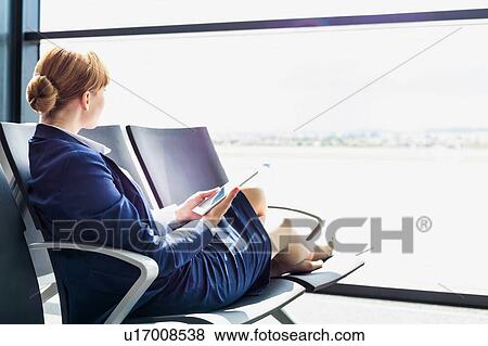 Young beautiful airport staff using digital tablet while sitting on chair during break View Large Photo Image Stock Photo - Young beautiful airport staff using digital tablet while sitting on chair during break . Fotosearch