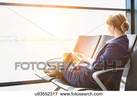 Young beautiful airport staff using digital tablet while sitting on chair during break View Large Photo Image Stock Photo - Young beautiful airport staff using digital tablet while sitting on chair during break . Fotosearch