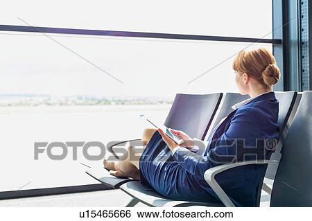 Young beautiful airport staff using digital tablet while sitting on chair during break View Large Photo Image Stock Photograph - Young beautiful airport staff using digital tablet while sitting on chair during break . Fotosearch